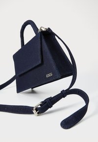 Marineblå håndtaske med en struktureret design, der har et kort håndtag, lang rem og et metallic logo på forsiden.