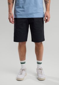 Black knee-length shorts with a smooth texture, paired with white sneakers and striped socks. The top is light blue cotton.