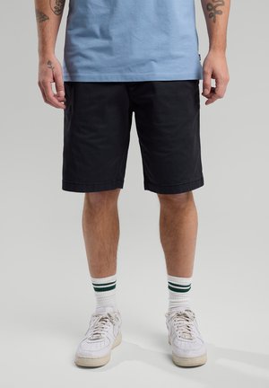 Black knee-length shorts with a smooth texture, paired with white sneakers and striped socks. The top is light blue cotton.