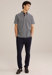 Joslas polo krekls tumši zilā un baltā krāsā, ar apkakli un trim pogām. Kombinēts ar pieguļošiem tumši ziliem biksēm un melnām kurpēm.