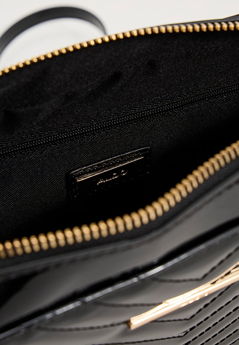 Intérieur d'un sac à main matelassé noir avec une texture lisse, une fermeture éclair dorée et une poche. Présente une étiquette de la marque à l'intérieur, mettant en avant un design élégant.