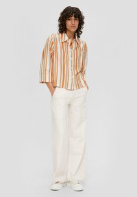 Gestreepte button-up shirt in oranje en wit, met een borstzak; gecombineerd met crèmekleurige wijde broek met zichtbare stiksels en zijzakken.