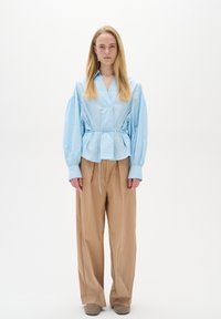 Light blue, long-sleeve shirt with a cinched waist and button closure, paired with beige, wide-leg trousers and beige shoes.