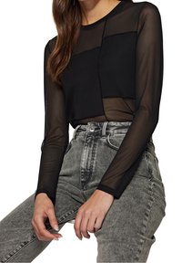 Black long-sleeve top with a sheer bodice and textured patch detailing, paired with high-waisted gray denim shorts featuring a button closure.