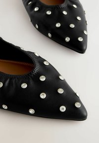 Svarta läderballerina med spetsig tå, prydda med metalliska detaljer och klara rhinestones jämnt fördelade på ytan och runt öppningen.