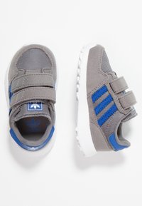 Harmaat urheilukengät, joissa siniset korostukset, valmistettu kankaasta ja synteettisistä materiaaleista. Varustettu tarranauhakiinnityksillä ja kuvioidulla kumipohjalla.