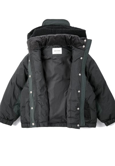 Veste matelassée noire pour enfants avec poignets élastiques, boutons-pression et une doublure douce et texturée au col, ouverte pour montrer l’étiquette intérieure.