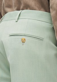 Ανοιχτό πράσινο παντελόνι ραμμένο με γλείσο τσέπη στο πίσω μέρος με κουμπί, συνδυασμένο με καφέ τοπ.