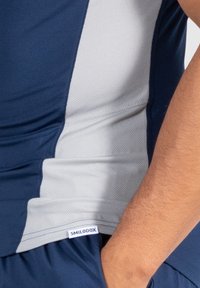 Námořnicky modré a šedé sportovní tričko s texturovaným povrchem a designem bočního panelu. Obsahuje malou bílou nálepku s nápisem "SMILODOX."