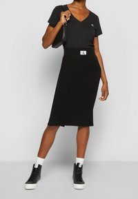 Černé midi šaty s V-výstřihem, ribbovanou texturou a přiléhavým pasem. Kombinováno s černými vysokými teniskami a malou černou kabelkou.