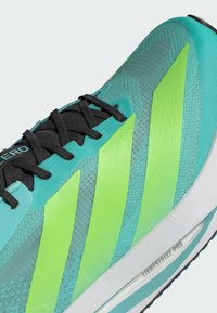 Scarpa da corsa turchese con strisce verdi, lacci neri, tomaia texturizzata e suola bianca etichettata "Lightstrike Pro."