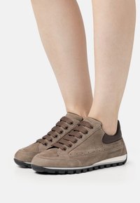Des baskets en daim marron présentent un bout arrondi, des lacets marron et une semelle en caoutchouc noir contrastante. Des accents latéraux affichent de petites perforations.