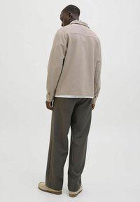 Lys beige oversized jakke med krave, parret med mørkegrå brede bukser og beige sko, set fra ryggen. Glat tekstur.