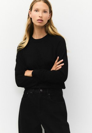 Svart fleece-tröja med rund halsringning och långa raglanärmar, tillsammans med högmidjade svarta jeans. Slät textur och minimalistisk design.