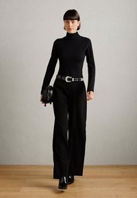 Top negro de cuello alto combinado con pantalones anchos negros. Cinturón plateado con tachuelas y bolso negro pequeño. Zapatos negros brillantes completan el look.