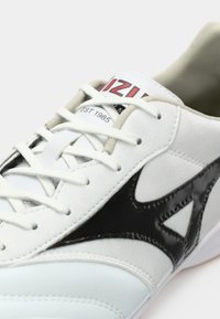 Witte sportschoen met zwarte accenten, gemaakt van glad leer en suede materialen, met een witte tussenzool en platte veters. Logo op de tong.
