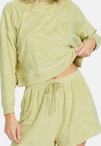 Svetle zelený set domácího oblečení s texturovaným designem s listovým vzorem. Vrchní část má dlouhé rukávy a zkrácený lem; šortky mají elastický pas.