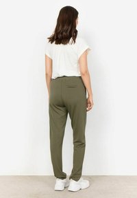Olive zelene jogger hlače z zadnjim žepom, narejene iz mehke tkanine, v kombinaciji z belim kratkotrajno majico. Model viden zadaj.
