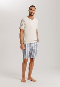 Hellbeige V-Ausschnitt-T-Shirt kombiniert mit blau-gestreiften Badehosen in verschiedenen Pastellfarben, mit Kordelzugbund und lockerer Passform.