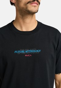 Black cotton t-shirt featuring "FUTURE MYTHOLOGY" in blue and "RVCA" in pink, set against a subtle patterned background. Short sleeves and crew neck.