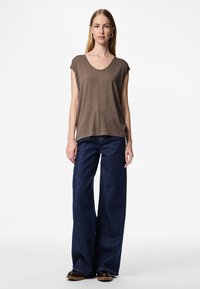 Ruskea lyhythihainen paita, jossa on pyöristetty pääntie, yhdistetty leveälahkeisiin tummansinisiin farkkuihin. Paidassa on teksturoitu kuvio ja rento istuvuus.