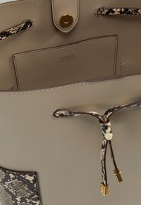 Beige läder bucket bag med slät textur, prydd med en kontrasterande ormtryckaccent, guldhardware och dragsnörning.