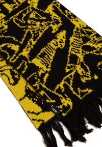 Sciarpa lavorata a maglia con un audace design giallo e nero, rifinita con frange. Il materiale sembra morbido con una finitura testurizzata. Etichetta del brand visibile.