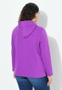Sudadera con capucha morada de textura suave. Presenta mangas largas, aberturas laterales en el dobladillo y un corte relajado.