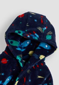 Kék bolyhos köntös kapucnival, színes űr témájú mintákkal, mint rakéták, bolygók és csillagok. Puha, texturált felület.
