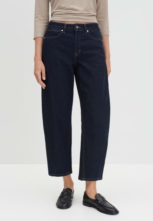 Donkerblauwe denim wijde pijp jeans met een hoge taille, voorzien van oranje stiksels en standaardzakken, gecombineerd met zwarte leren instapschoenen.
