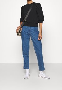 Black puff-sleeve sweater paired with straight-leg blue jeans and white high-top sneakers. Accessories include a small leopard-print crossbody bag.