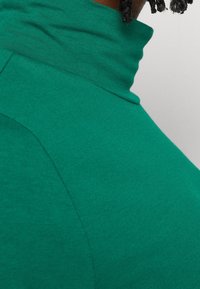 Grön polotröja i en mjuk, strukturerad tyg. Har en hög krage och böjda sömmar för en figurnära silhuett.