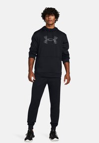 Sort hættetrøje og matchende joggers lavet af blødt stof. Har et stort logo på brystet og elastiske manchetter ved anklerne.