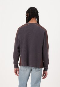Langærmet, tofarvet pullover i mørkegrå og brun, med ribbet struktur, rund halsudskæring og afslappet pasform, med synlige sømdetaljer.