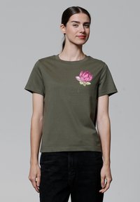Olivegrünes Baumwoll-T-Shirt mit einem pinken Lotusblumen-Graphic auf der linken Brust. Lässiger Schnitt mit kurzen Ärmeln und Rundhalsausschnitt.