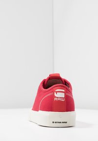 Basket en toile rouge avec semelle en caoutchouc blanche. Équipée d'un onglet de talon en boucle et d'un logo blanc à l'arrière. Design simple avec des accents de couture.