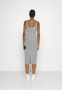 Robe midi à rayures noires et blanches avec un dos échancré, une coupe ajustée et une fente latérale, associée à des baskets blanches.