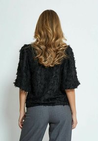 Top nero texturizzato con maniche corte, caratterizzato da un design a strati; abbinato a pantaloni grigi, che mettono in risalto il motivo intricato del top.