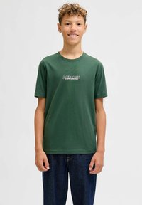 Groene katoenen t-shirt met korte mouwen, voorzien van een centraal wit logo. Gecombineerd met donkerblauwe denimbroek, beide in een relaxte pasvorm.