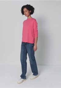 Suéter de punto rosa con mangas largas, combinado con jeans azules de pierna recta y zapatillas blancas. Diseño sencillo con puños y dobladillo acanalados.