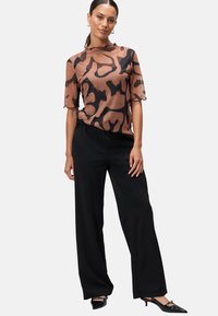 Haut transparent marron avec des motifs noirs abstraits, manches courtes et bords en dentelle, associé à un pantalon large noir taille haute.