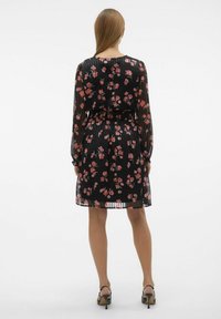 Svart plisserad klänning med blommönster i rosa och röd, långa ärmar, åtsittande midja och utsvängd nederdel. Slät textur, mjukt tyg.