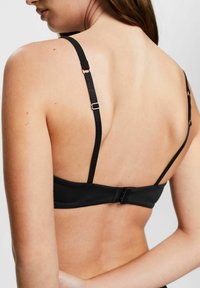 Black bra with adjustable straps, smooth fabric, and a hook closure. The design features minimalistic detailing and a comfortable fit.