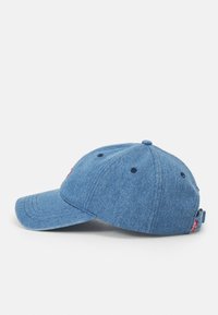 Gorra de béisbol de color azul denim con visera curvada, correa ajustable, ojales de ventilación y un parche con logo en la parte frontal.