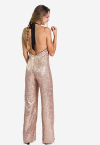 Combinaison en sequins rose doré avec un col halter, dos nu, design à jambes larges et détail en ruban noir. Texture lisse et finition brillante.
