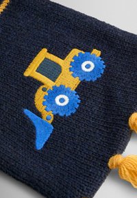 Tamsiai mėlynas audinys su išsiuvinėtu gelsvu traktoriaus raštu, su mėlynomis ratukais ir mėlynu peiliu, iš šonų kabinėjosi oranžinės kutai.