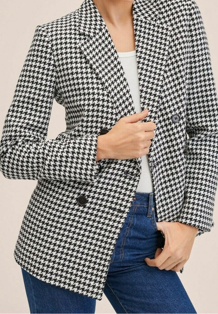 Blazer a fantasia houndstooth bianco e nero, doppiopetto con due bottoni, colletto a punta, abbinato a una maglietta bianca e jeans.