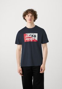 T-shirt in cotone blu navy con una grafica audace in rosso e bianco, con il testo "JACK & JONES" e l'anno di fondazione al centro.