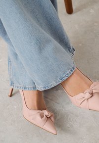 Rosa läder högklackade skor med spetsig tå och en dekorativ rosett. Bärs tillsammans med ljusblå vida jeans.