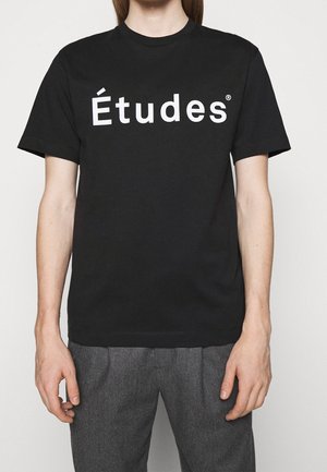 T-shirt en coton noir avec un logo "Études" blanc audacieux sur la poitrine. Encolure ronde, manches courtes et coupe décontractée.